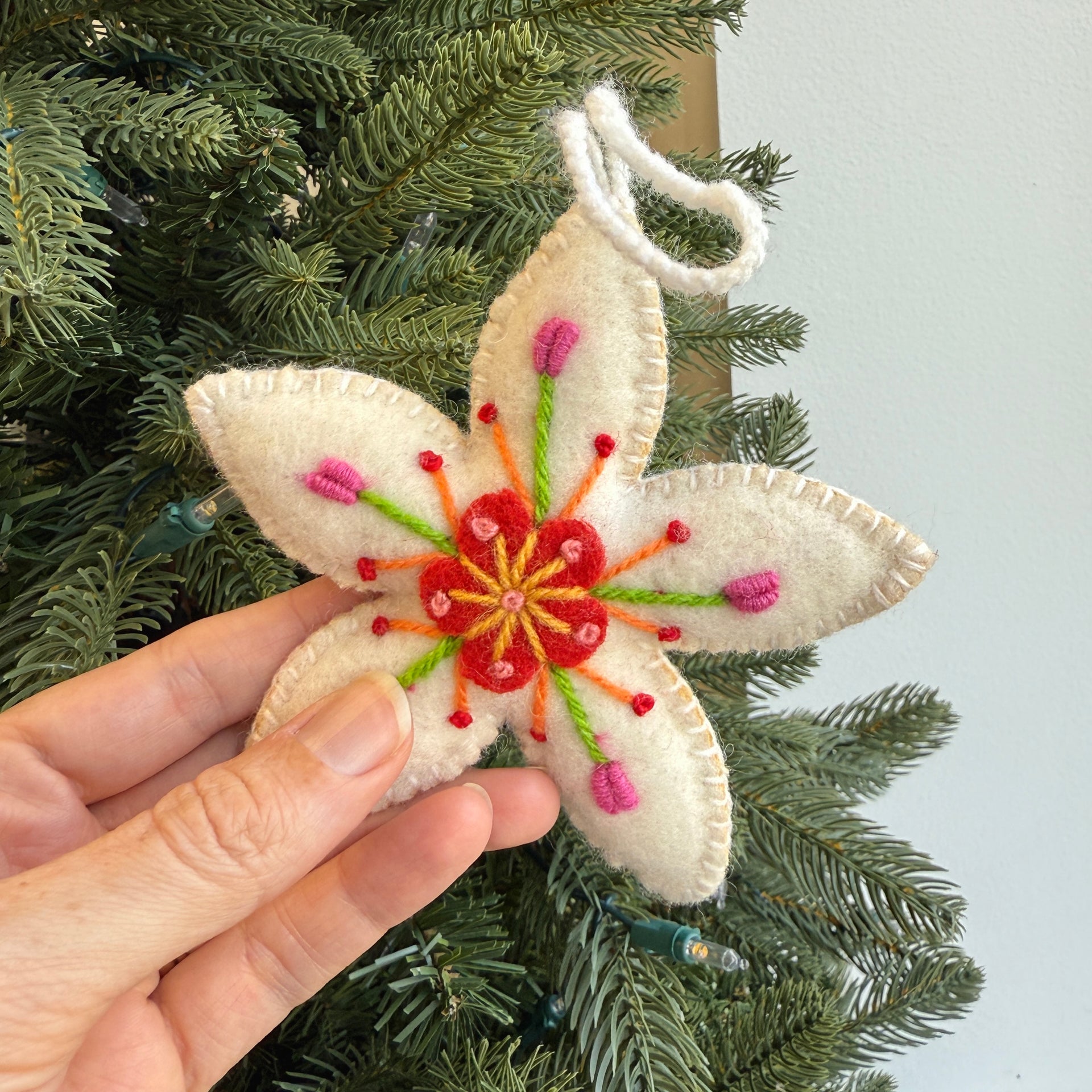 Hand holding a felt wool embroidered flower ornament against a Christmas tree background