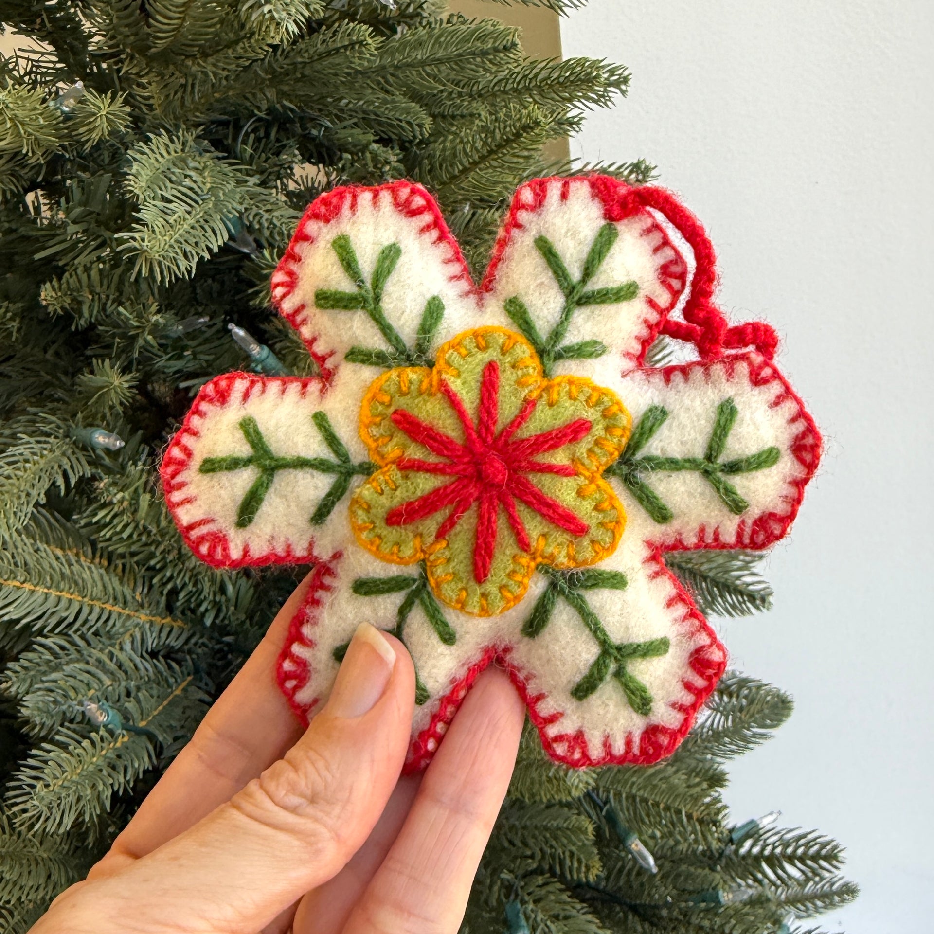 Hand holding a felt snowflake ornament with greenery in the background