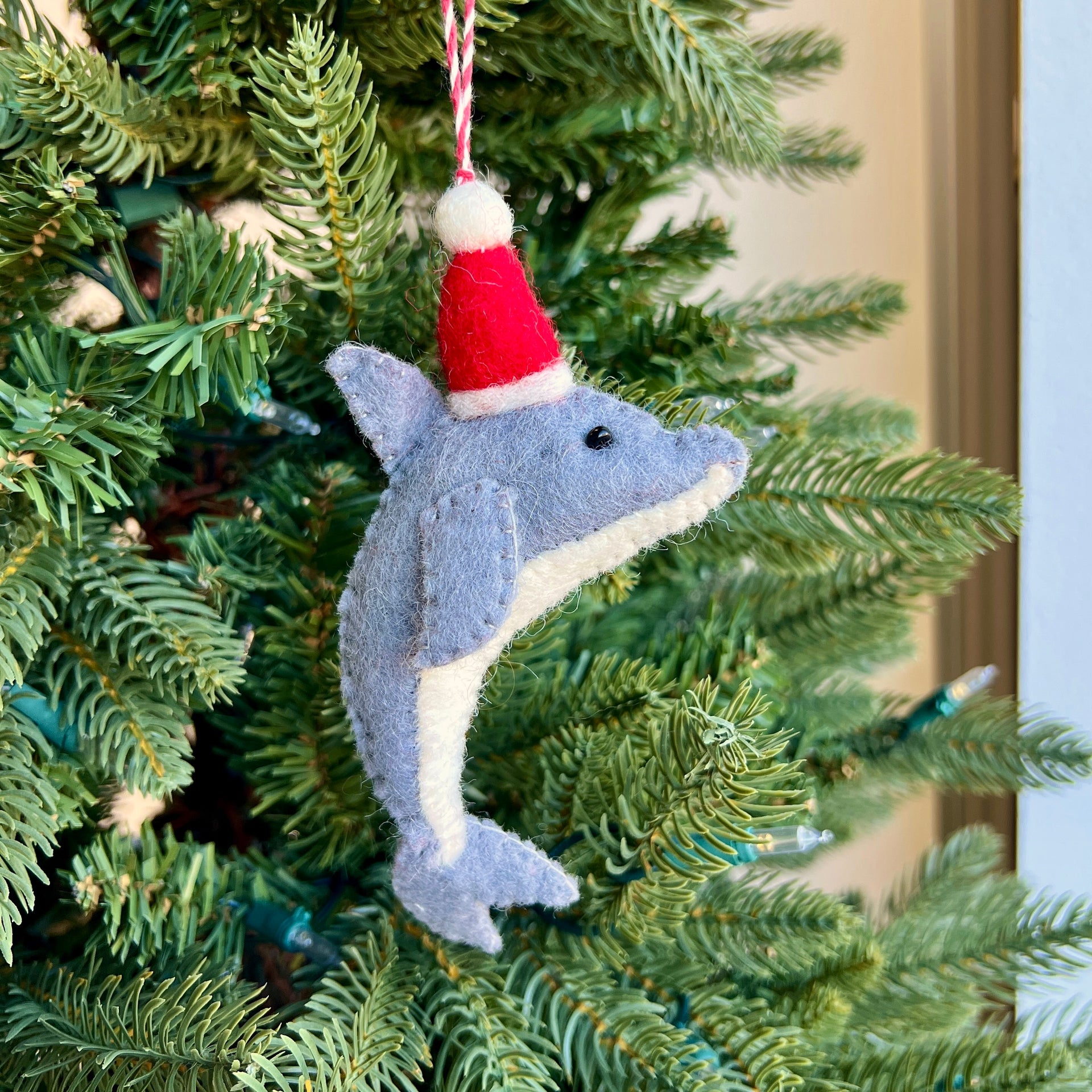 Dolphin ornament with a Santa hat hanging on a Christmas tree.