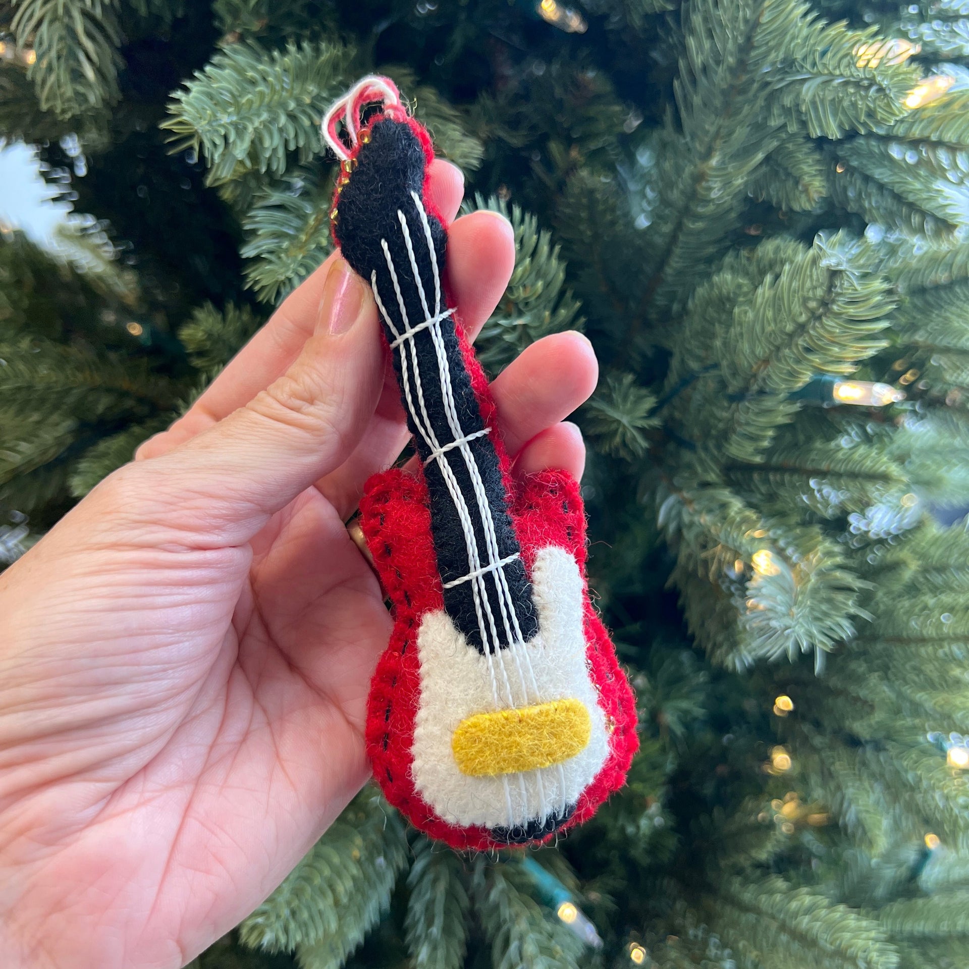 Red electric guitar ornament held up by a Christmas tree.