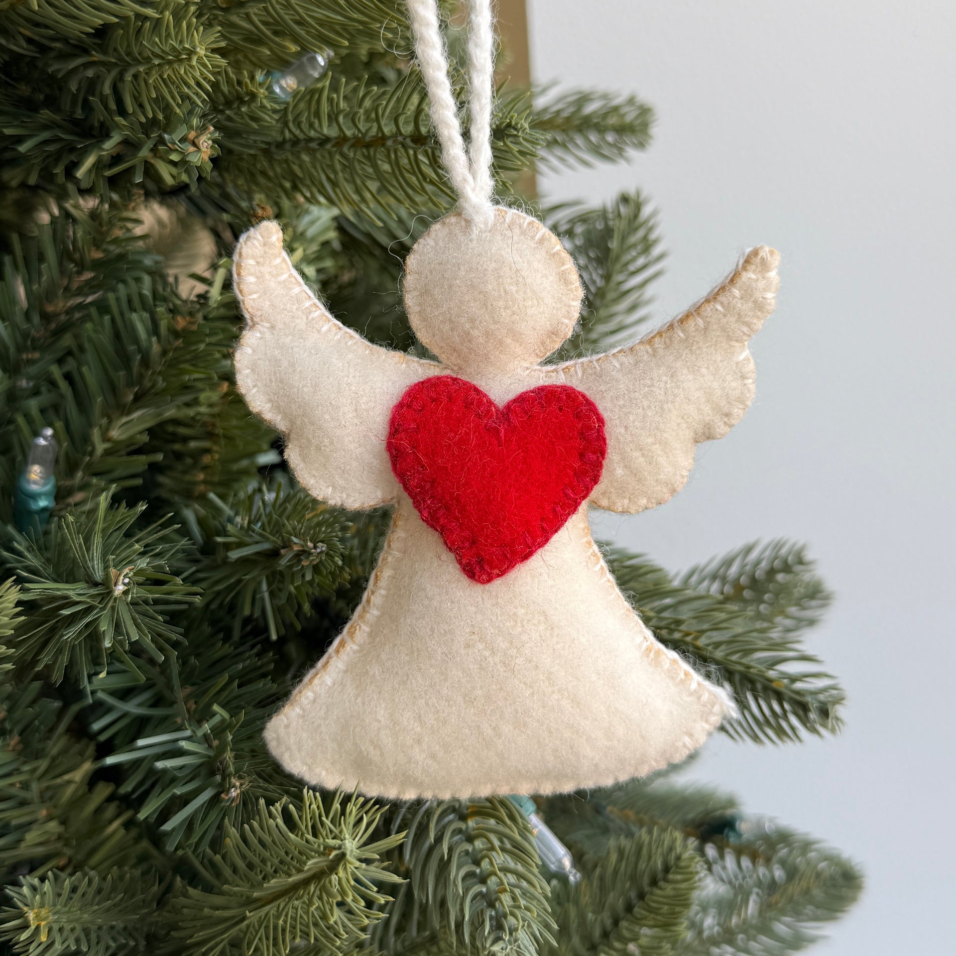 Felt angel ornament with a red heart hanging on a Christmas tree.