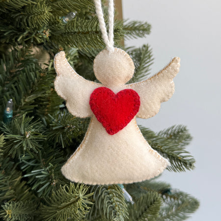 Felt angel ornament with a red heart hanging on a Christmas tree.
