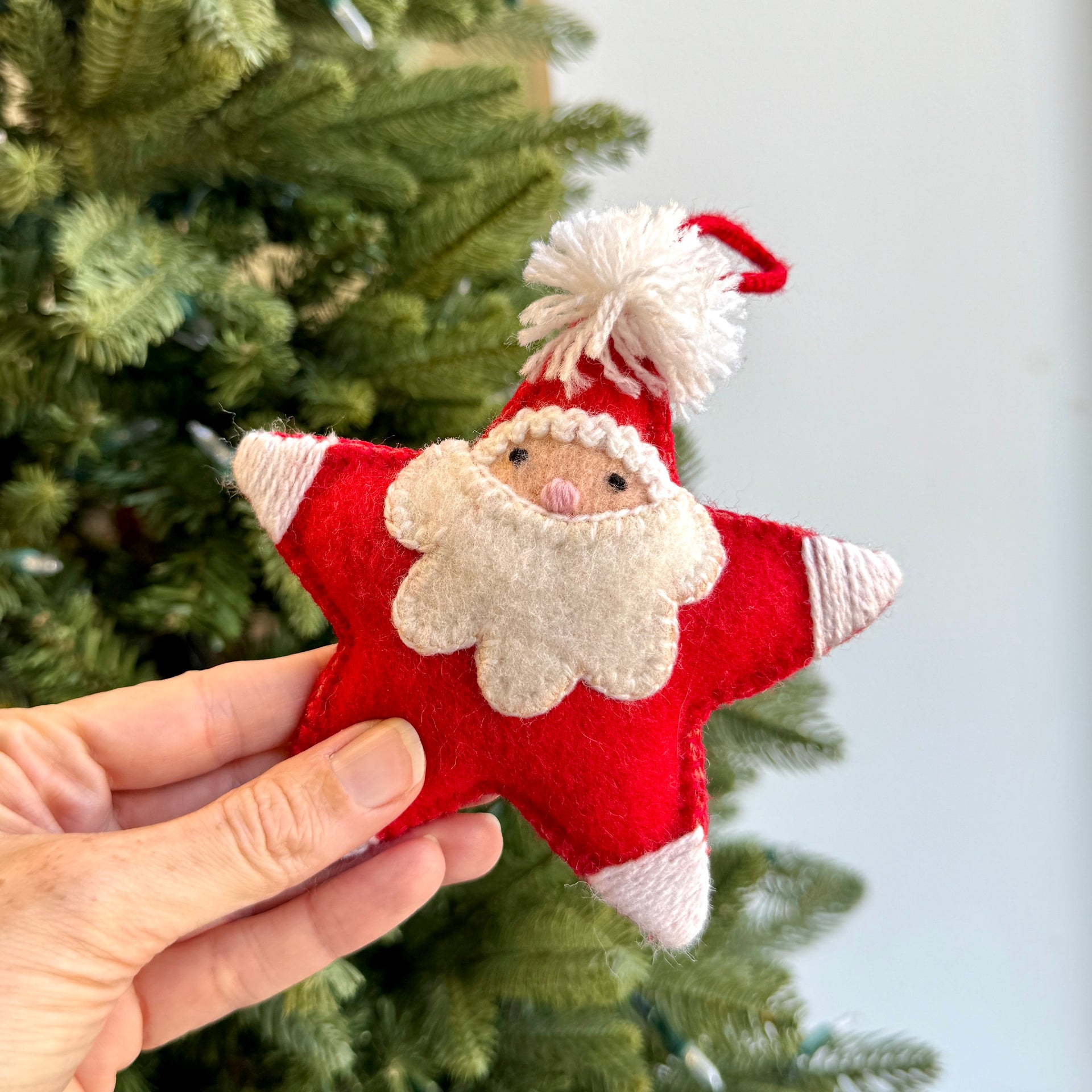 Star-shaped Santa Claus ornament held in front of a Christmas tree.