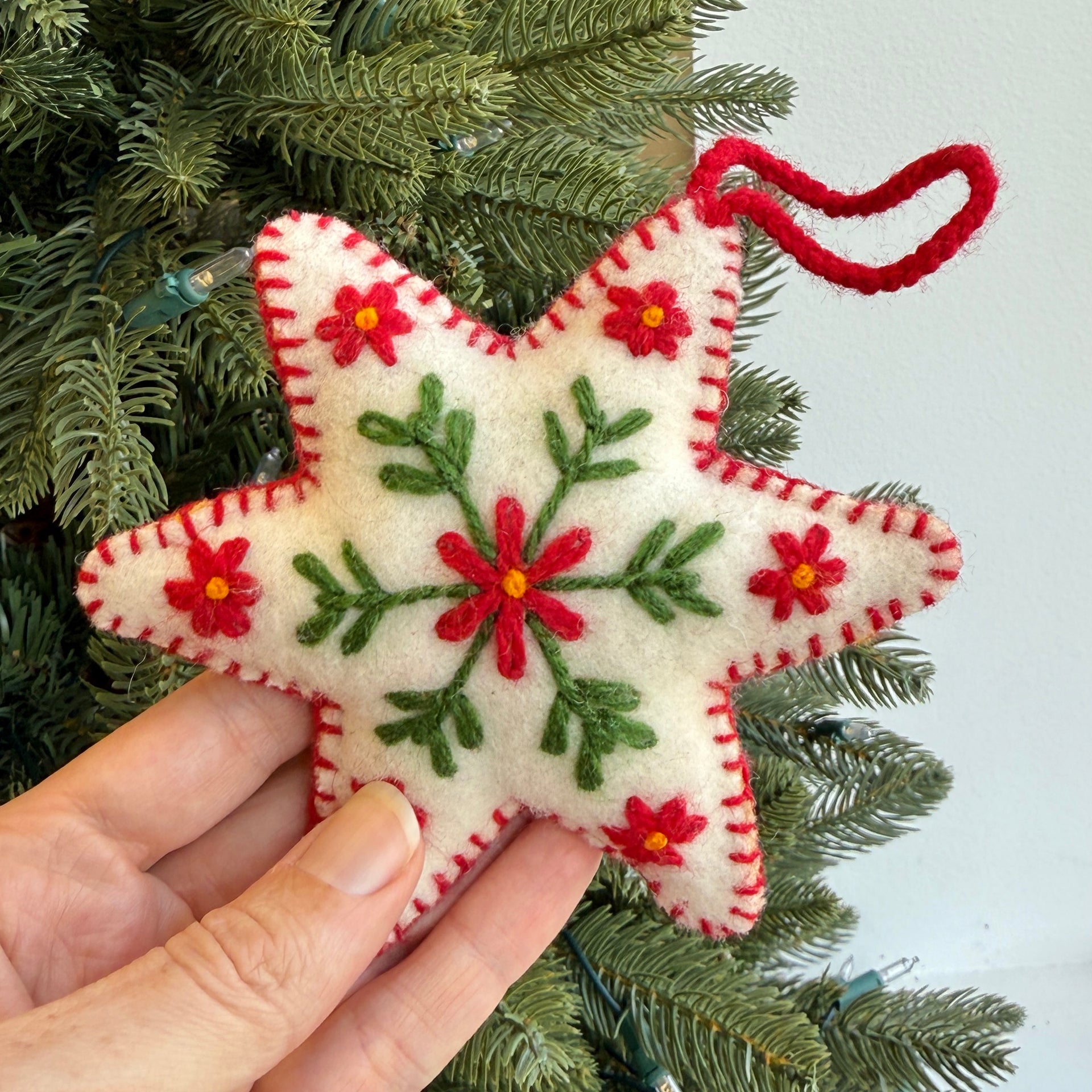 Star-shaped embroidered ornament with red flowers and green leaves, held against a Christmas tree.