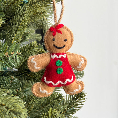 Felt gingerbread girl ornament with a red dress hanging on a Christmas tree.