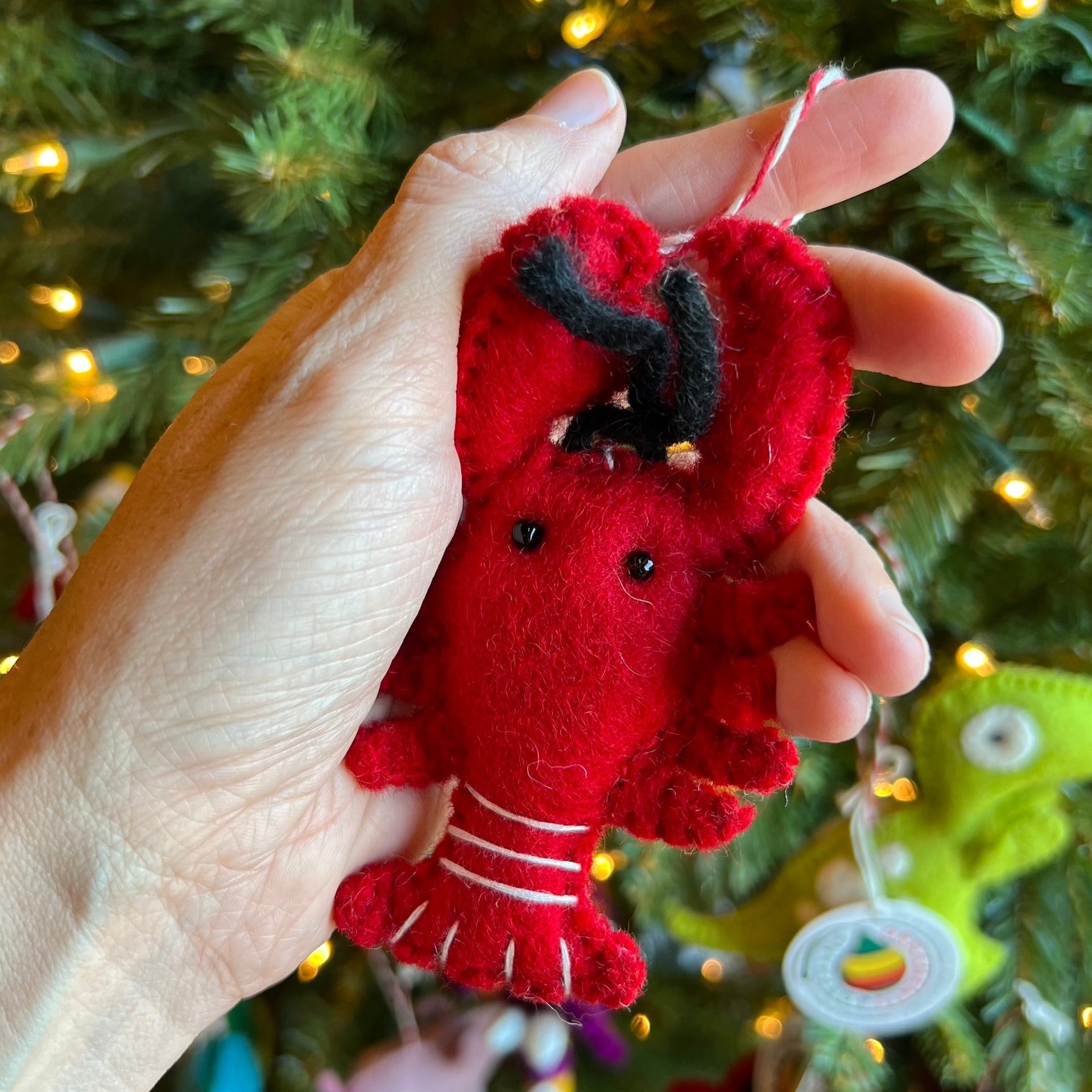 felt lobster ornament being held in front of a Christmas tree