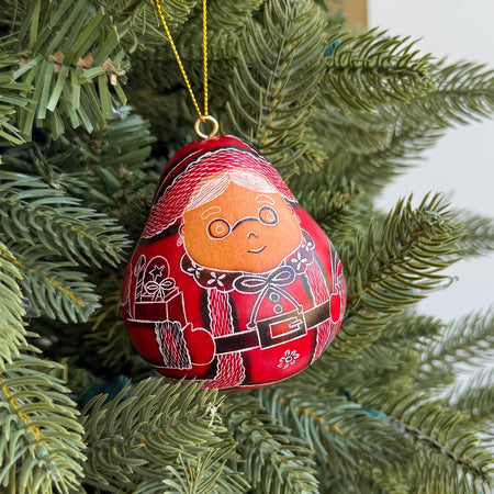 Decorative gourd Christmas ornament shaped like Mrs. Claus, featuring a face and red outfit, hanging on a tree.