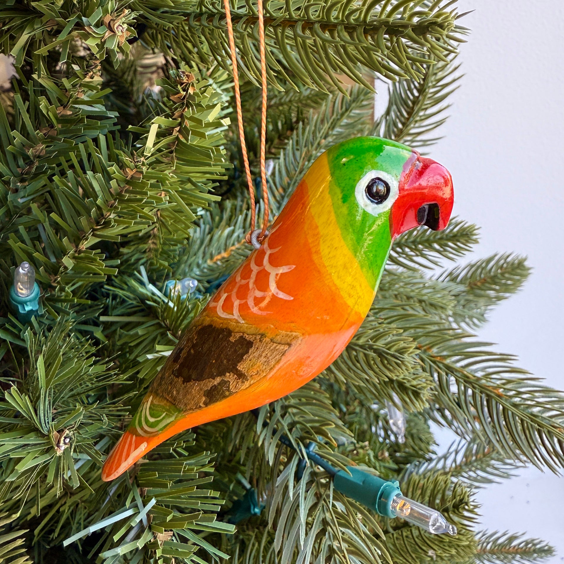 Colorful orange parrot ornament hanging on a Christmas tree