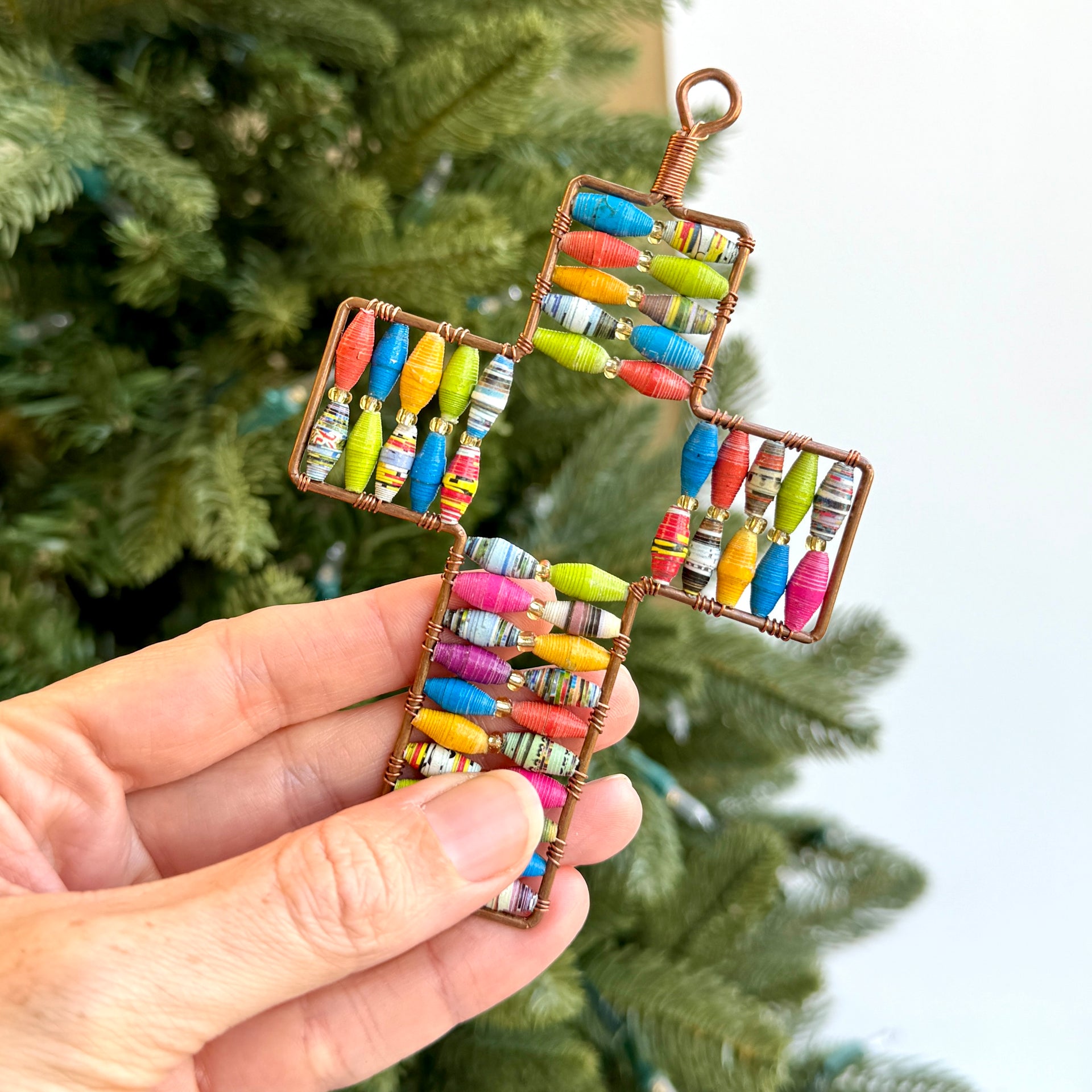 Colorful cross shaped ornament held by a hand with a Christmas tree in the background