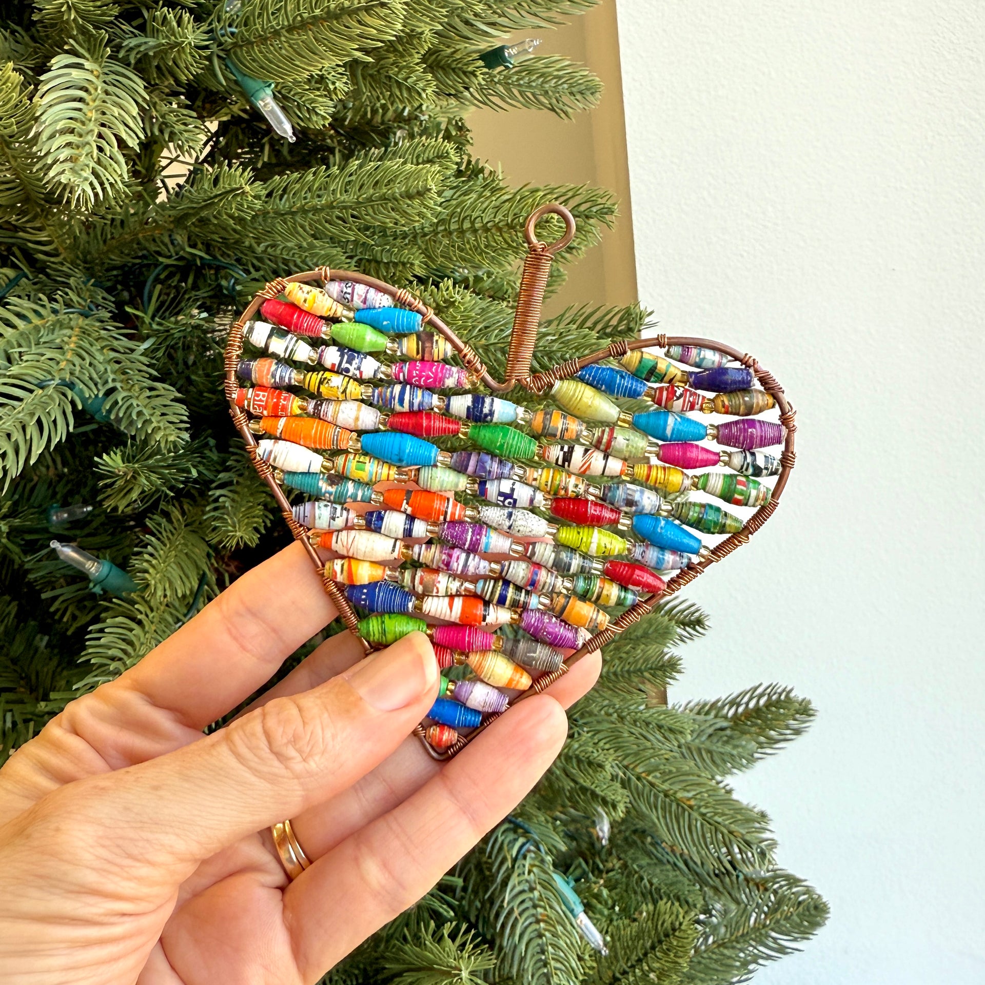 Heart-shaped ornament with colorful beads held in front of a Christmas tree.