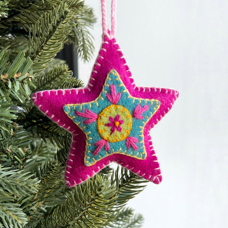 Colorful star-shaped Christmas ornament hanging on a tree branch.