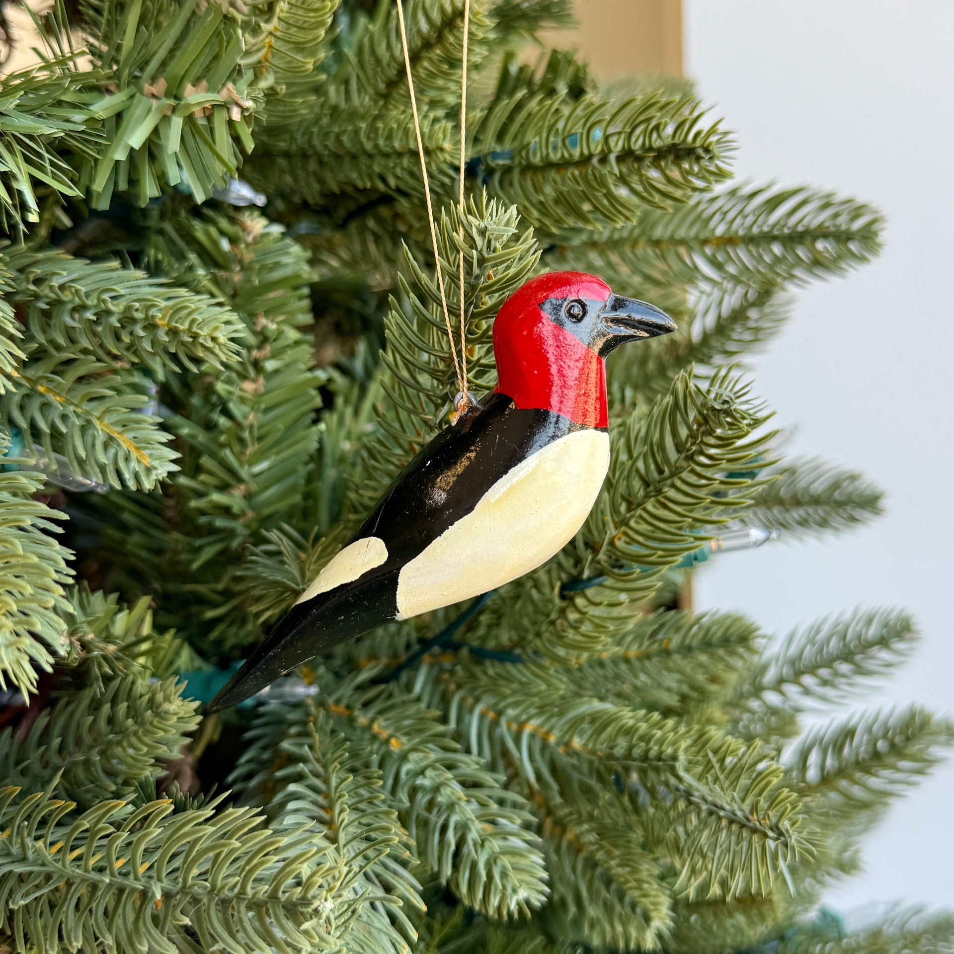 Decorative bird ornament with red and black head hanging on a Christmas tree.
