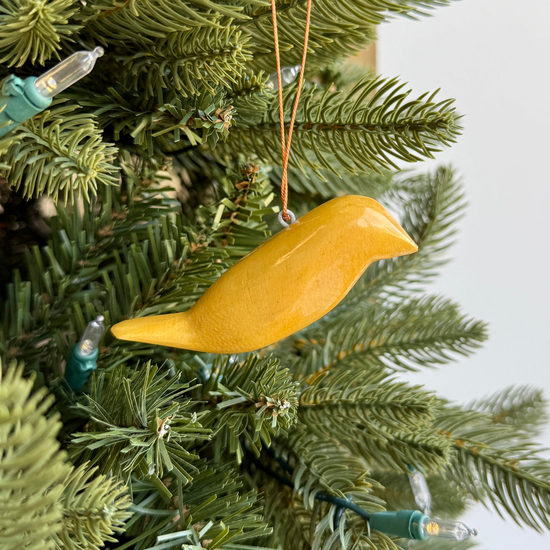 Varnished bird ornament hanging on a Christmas tree with green branches and lights.