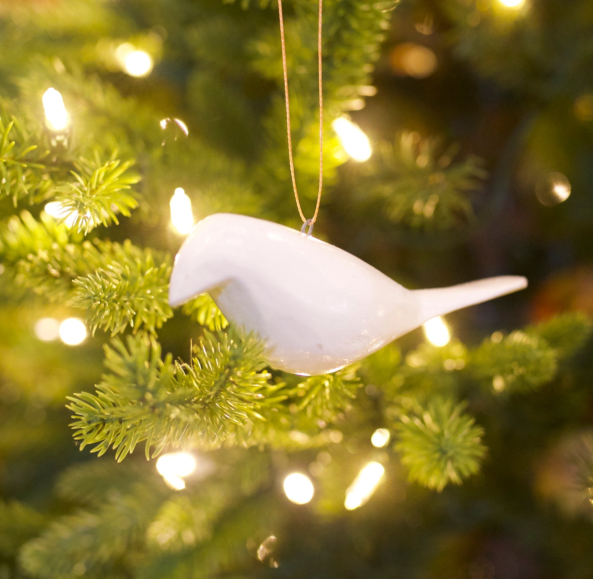 White wooden bird ornament hanging on a Christmas tree with lights.