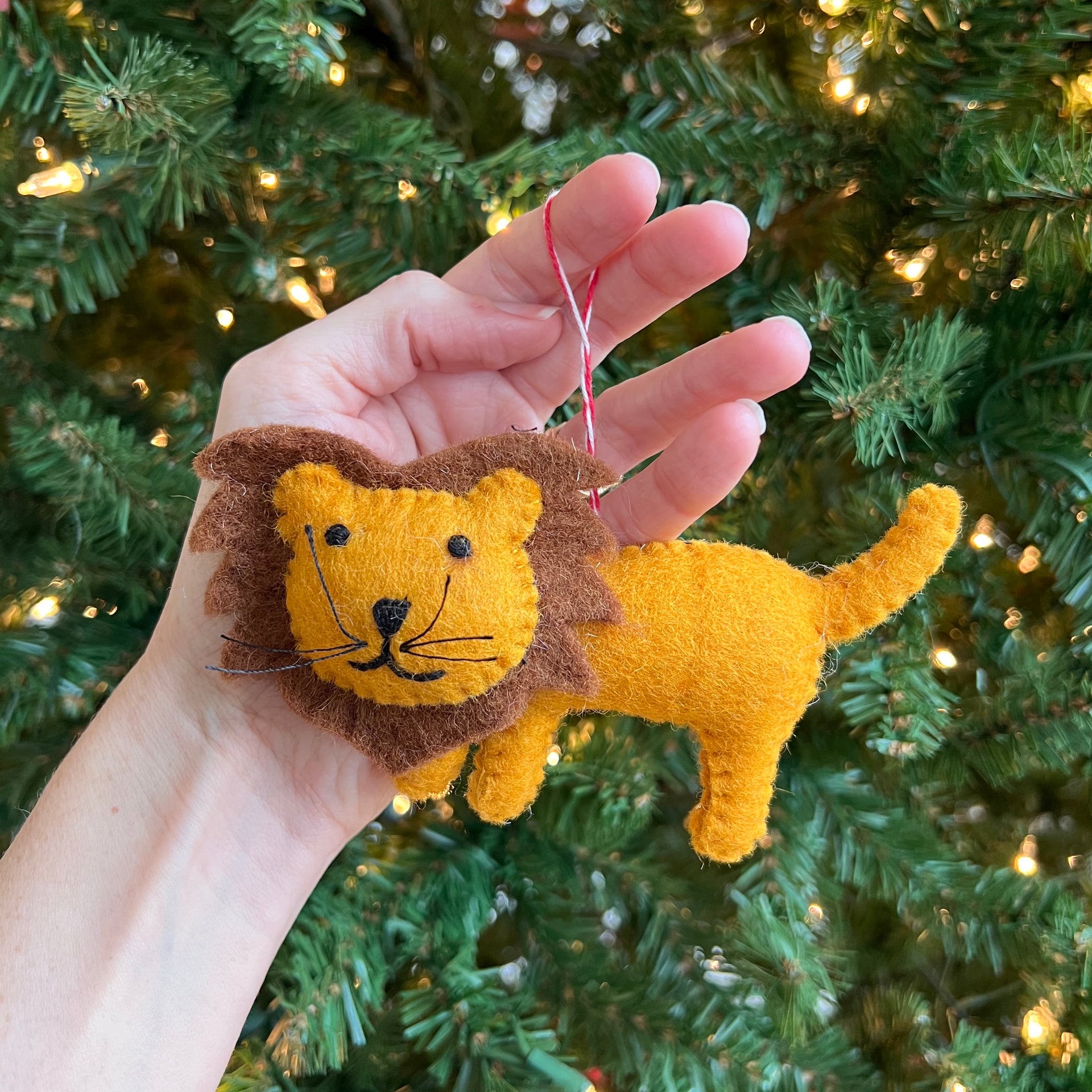 Hand holding a lion-shaped ornament in front of a decorated Christmas tree.