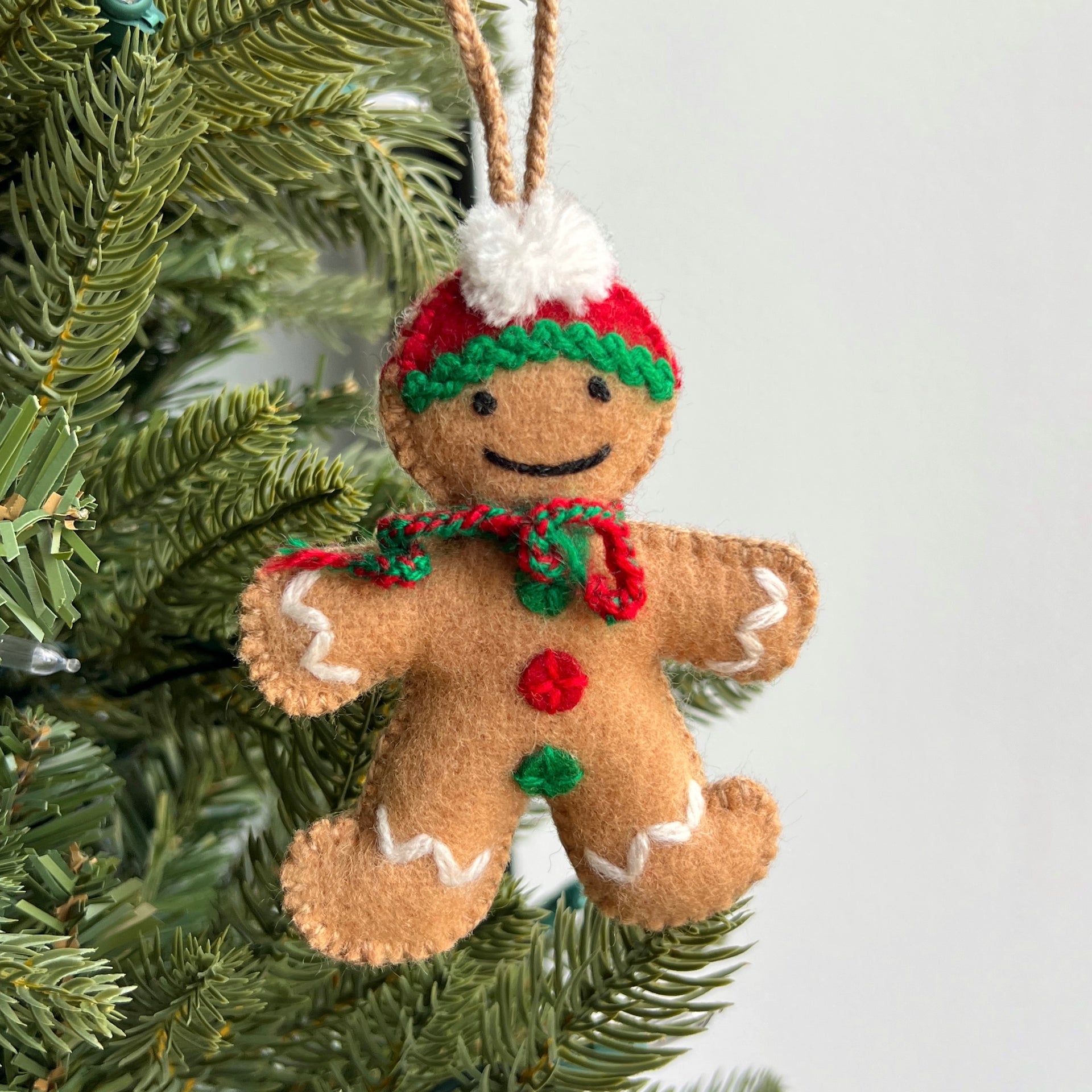 Felt gingerbread man ornament with a hat and scarf hanging on a Christmas tree.