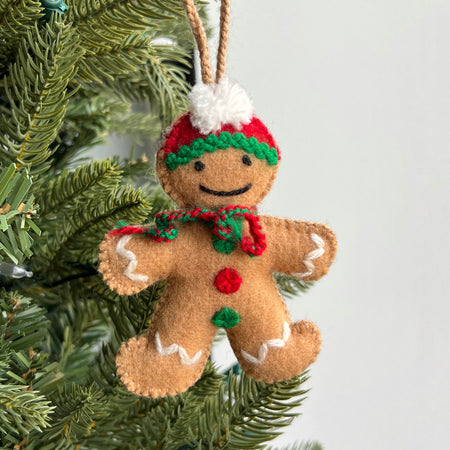 Felt gingerbread man ornament with a hat and scarf hanging on a Christmas tree.
