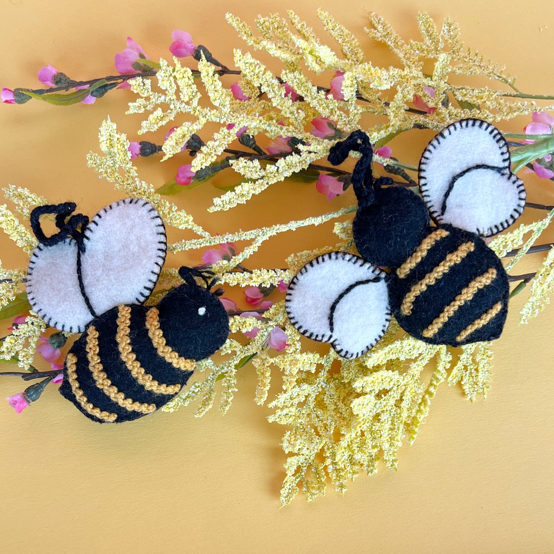 Two embroidered bee ornaments resting on yellow flowers.